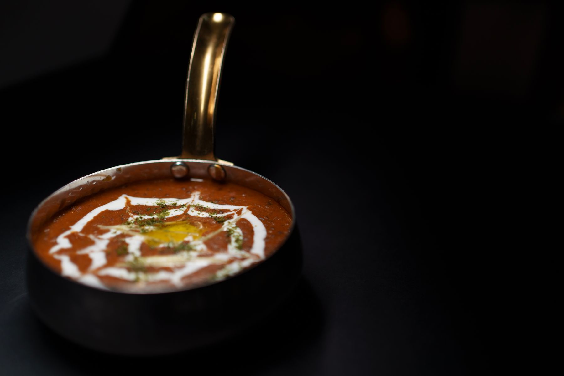 Dal makhani in a brass-handled pan against a dark background