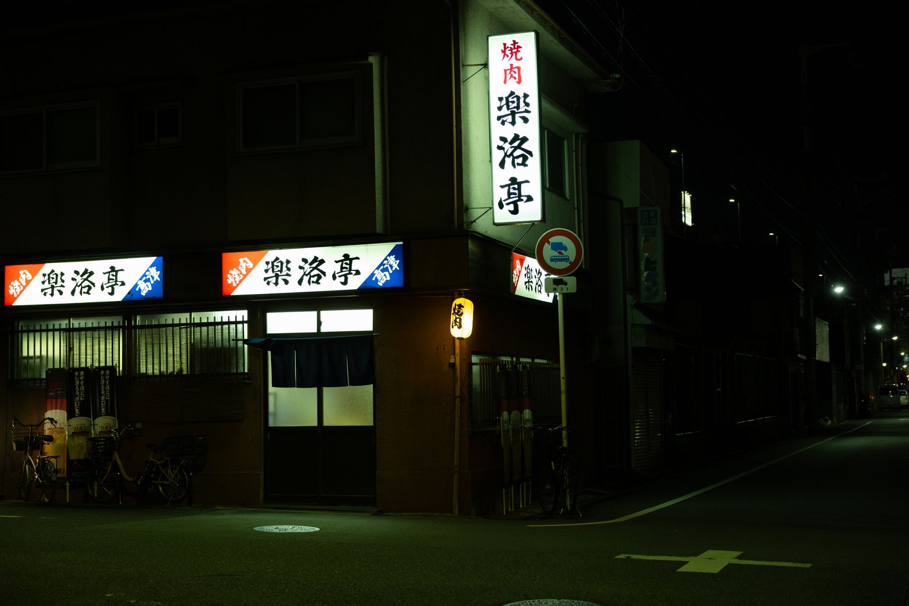 Lantern-lit Japanese restaurant on a dark street corner at night