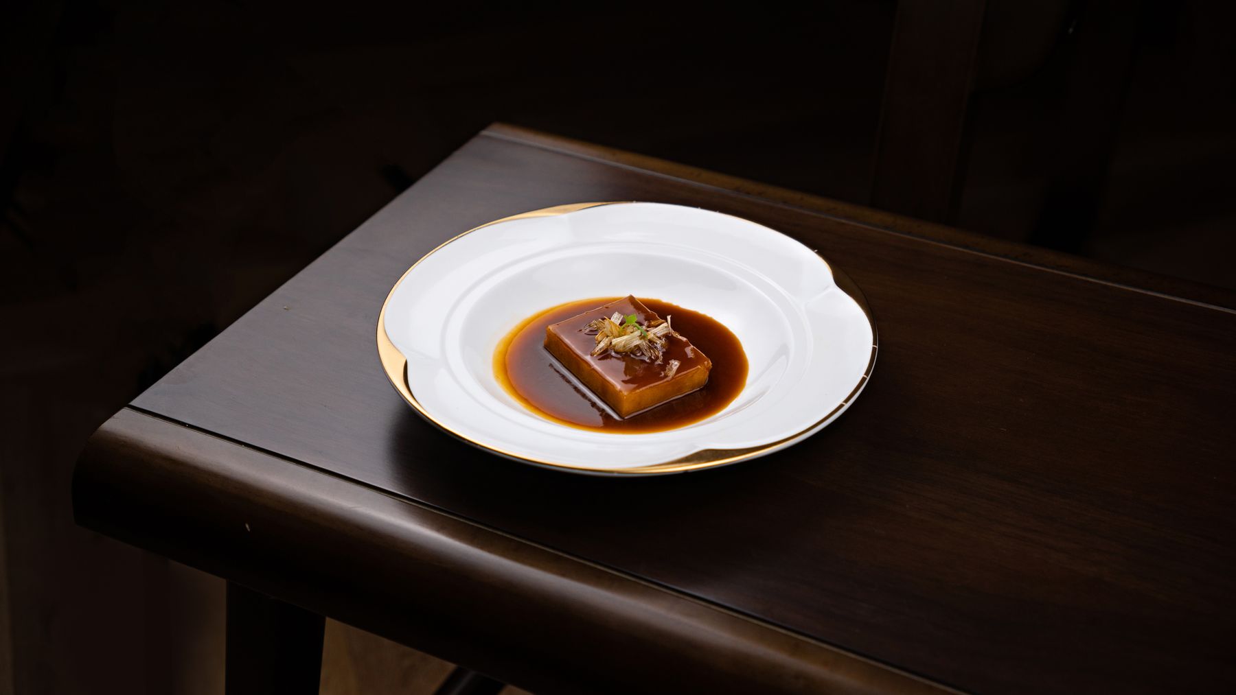 Glazed dessert on a gold-rimmed plate against dark wood