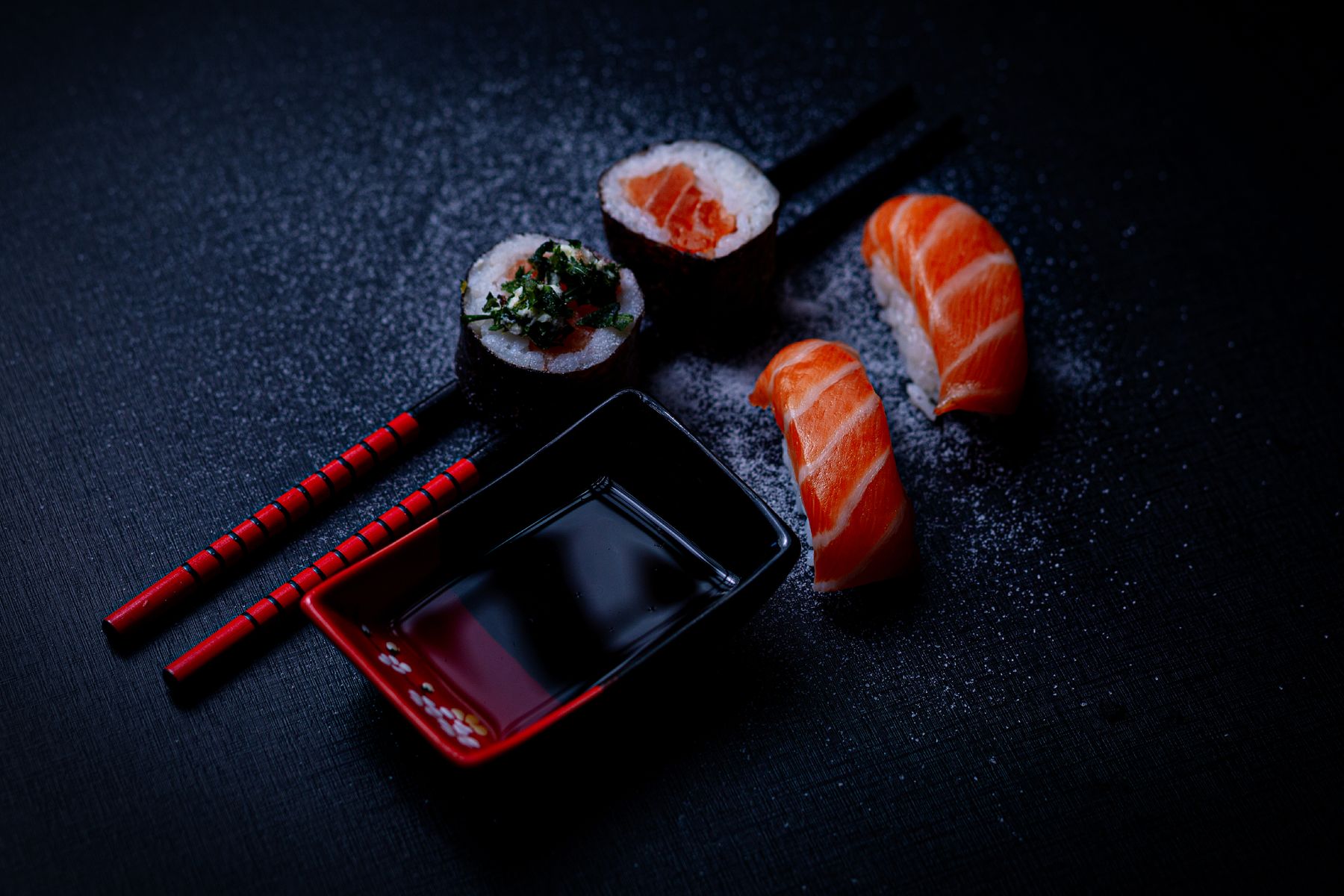 Salmon sushi with soy sauce and chopsticks on dark slate