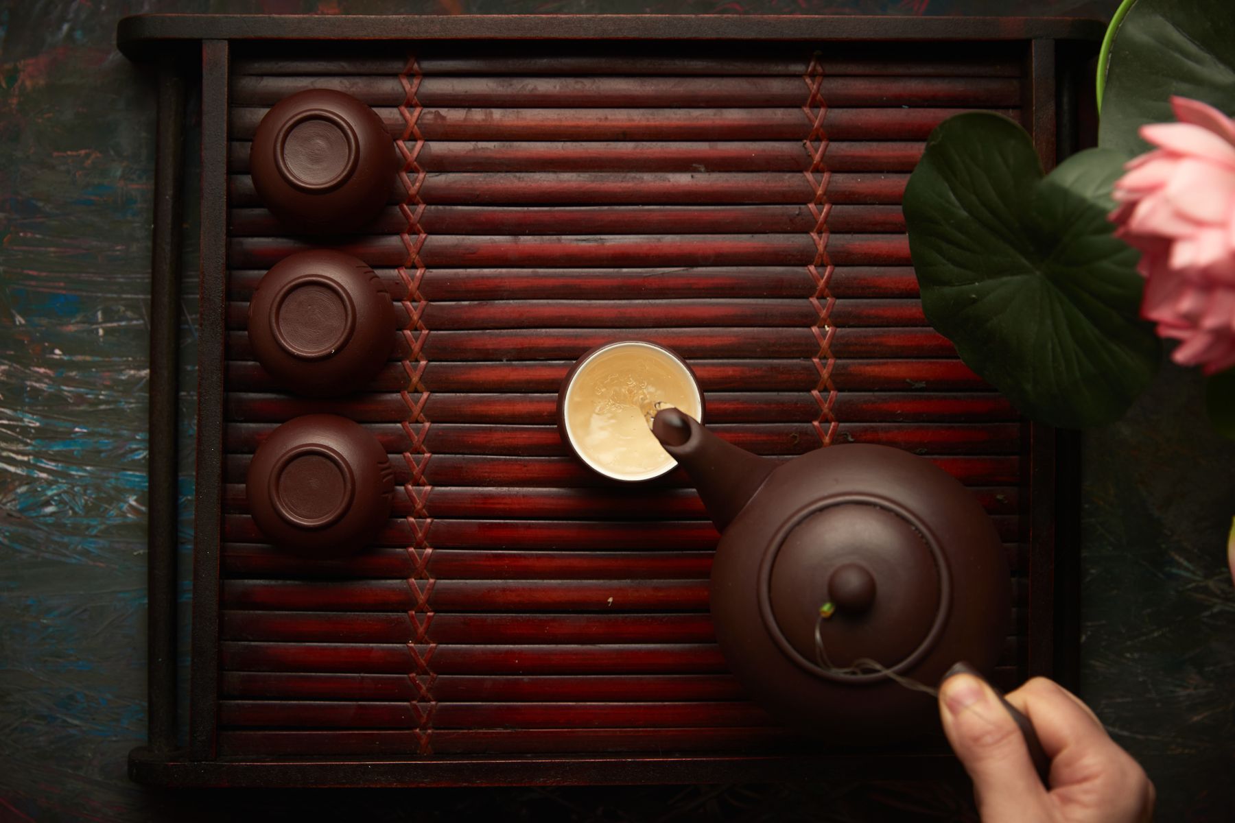 Tea poured from a clay teapot on a dark bamboo tray
